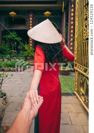 couple's trip to Asia in Vietnam. Follow me with the back of a female traveler tourist in Vietnamese hat at a temple in Vietnam in Asia 124529138
