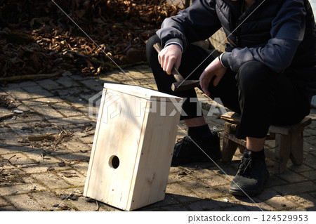 A man crafts a wooden birdhouse outside, preparing a cozy spring home for birds in the garden. A man crafts a wooden birdhouse outside, preparing a cozy spring home for birds in the garden. 124529953