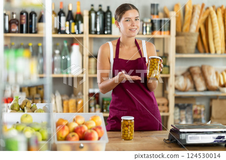Young woman seller offering olives in grocery store 124530014