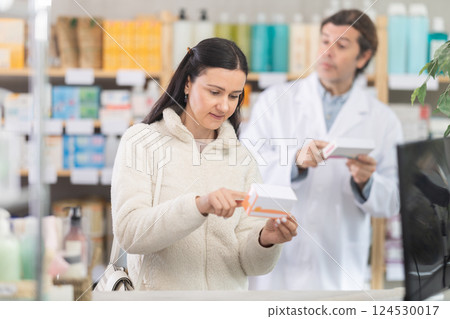 Woman chooses pills in modern pharmacy. Male pharmacist helps with choosing medicine 124530017