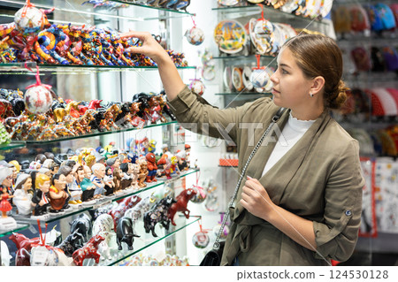 Curious female tourist looking to buy ceramic figurines at souvenir shop 124530128