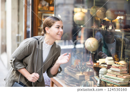 Cheerful female tourist inspecting merchandise through window of antiques shop Cheerful female tourist inspecting merchandise through window of antiques shop 124530160