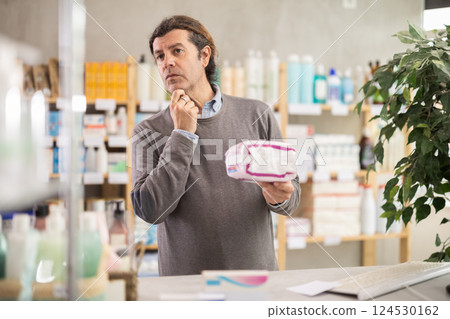 In drug store, man examine feminine pads packaging In drug store, man examine feminine pads packaging 124530162