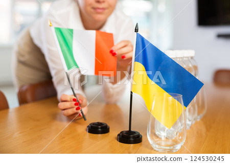 Flags of Ukraine and Italy in female hands preparing negotiating table 124530245