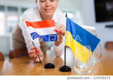 Female hands arranging flags of Netherlands and Ukraine on negotiating table Female hands arranging flags of Netherlands and Ukraine on negotiating table 124530275