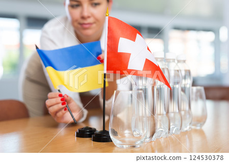 Little flag of Switzerland on table and flag of Ukraine put next to it by young woman Little flag of Switzerland on table and flag of Ukraine put next to it by young woman 124530378