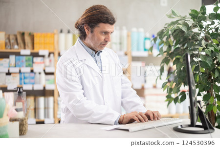 Pharmacist in uniform looking for medicine in pharmacy using computer Pharmacist in uniform looking for medicine in pharmacy using computer 124530396