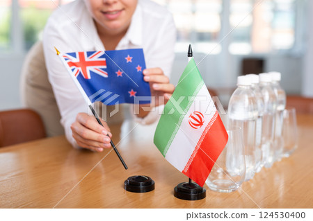 Woman secretary prepares an office for negotiations - she places flags of Iran and Australia table Woman secretary prepares an office for negotiations - she places flags of Iran and Australia table 124530400