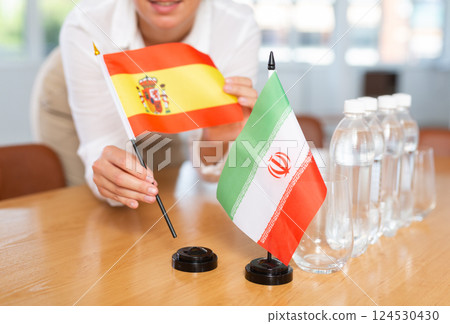 Woman secretary prepares an office for negotiations - she places flags of Spain and Iran table 124530430