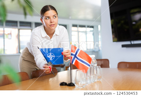 Young lady sets miniatures flags of Norway and NATO for international negotiations Young lady sets miniatures flags of Norway and NATO for international negotiations 124530453