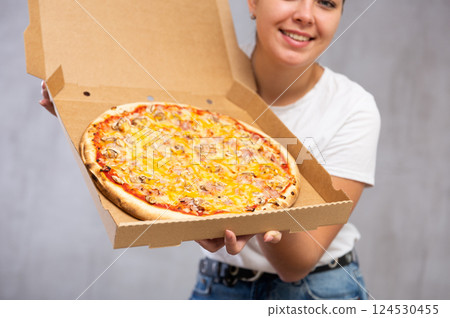 Photo of pizza held by smiling young woman against gray background 124530455