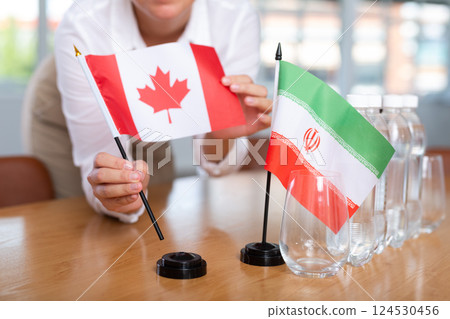 Little flag of Iran on table and flag of Canada put next to it by young woman Little flag of Iran on table and flag of Canada put next to it by young woman 124530456