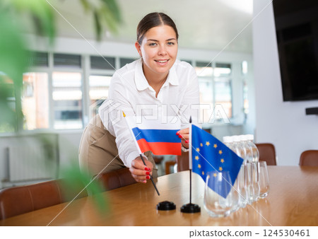Woman secretary prepares an office for negotiations - she places flags of European Union and Russia table 124530461