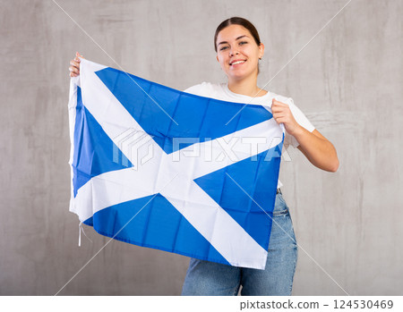 Happy young female student with flag of Scotland against gray wall background indoors Happy young female student with flag of Scotland against gray wall background indoors 124530469