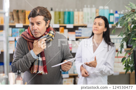 man with a scarf tied around his throat stands in a pharmacy against the background of pharmacist man with a scarf tied around his throat stands in a pharmacy against the background of pharmacist 124530477