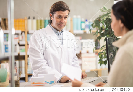 male pharmacist stands behind the counter near the computer and communicates with a customer male pharmacist stands behind the counter near the computer and communicates with a customer 124530490