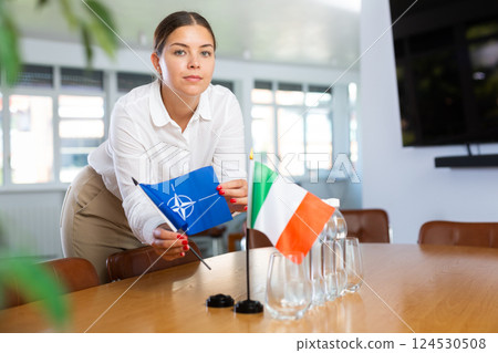 Employee of delegation prepares negotiating table - sets up flag of NATO (OTAN) and Italy 124530508