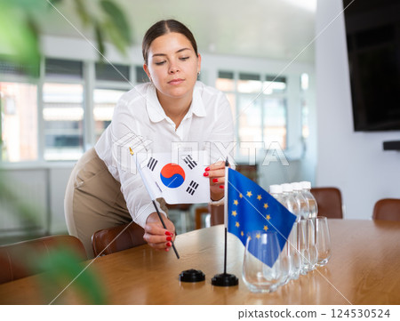 Young woman puts South Korea and EU flags on table in office 124530524