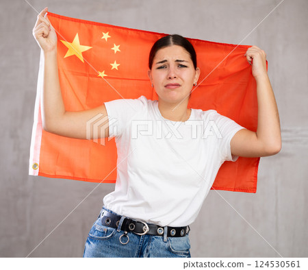 Sad young woman holding China flag against unicoloured background 124530561