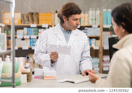 male pharmacist stands behind the counter near the computer and communicates with a customer male pharmacist stands behind the counter near the computer and communicates with a customer 124530562