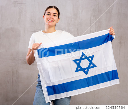 Contented young woman holding Israel flag against unicoloured background Contented young woman holding Israel flag against unicoloured background 124530564