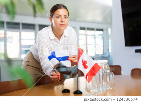 Young woman putting flags of Finland and Canada on table in office 124530574