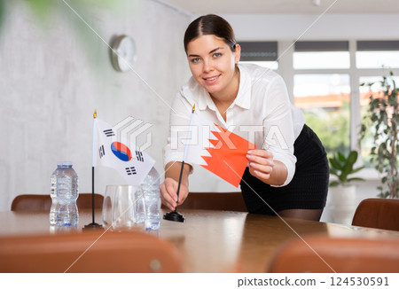 Young female attendant putting up flags for international negotiations between south korea and bahrain 124530591