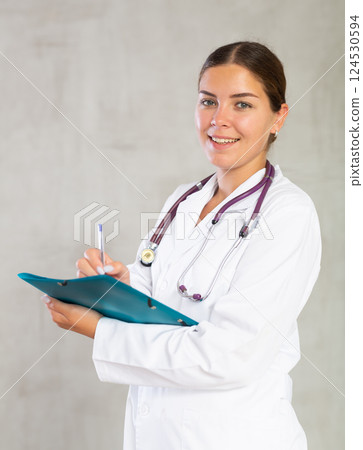 Female doctor makes notes in documents holding a folder of papers in her hands 124530594