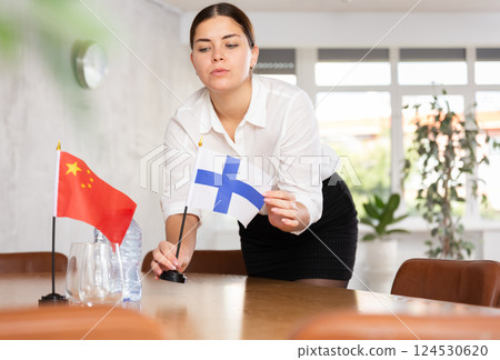 Preparing for business negotiations - woman sets small flags of countries of China and Finland on table Preparing for business negotiations - woman sets small flags of countries of China and Finland on table 124530620