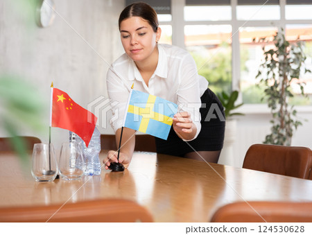 Preparing for business negotiations - woman sets small flags of countries of China and Sweden on table 124530628