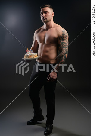 Celebrating a birthday with a fit man holding a cake in a studio setting Celebrating a birthday with a fit man holding a cake in a studio setting 124531253