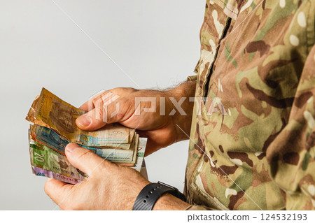 Soldier holding various banknotes in military uniform 124532193