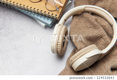 Wireless headphones, eyeglasses and notebooks resting on cozy sweater 124532641