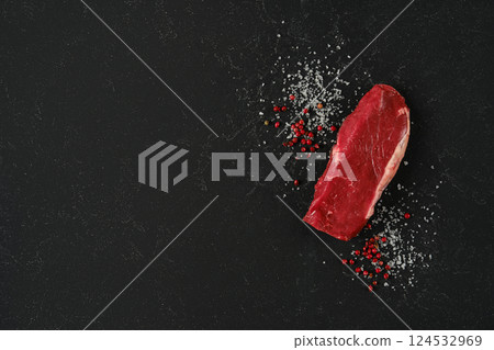 Fresh raw beef sirloin steak with spices on dark stone countertop ready for cooking 124532969