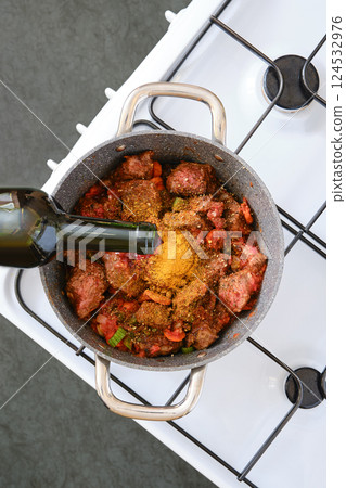 Cooking a savory dish with meat, spices, and vegetables in a pot on a modern stove 124532976