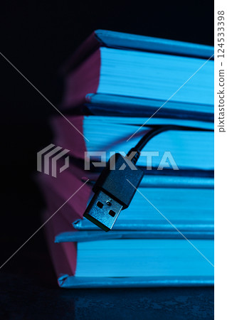 Books with a black USB cable on a dark background. 124533398