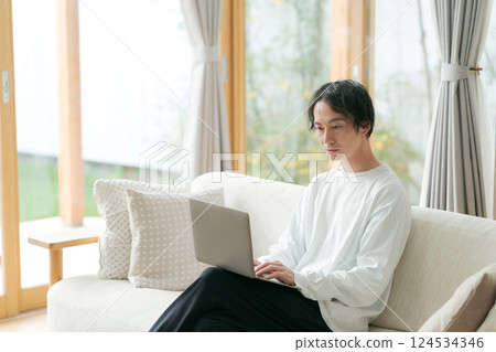 Man sitting on sofa using computer Man sitting on sofa using computer 124534346