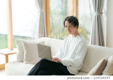 Man sitting on sofa using computer Man sitting on sofa using computer 124534347