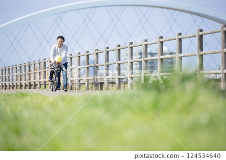 A child and his father practice riding a bicycle along the river. Good luck! A child and his father practice riding a bicycle along the river. Good luck! 124534640