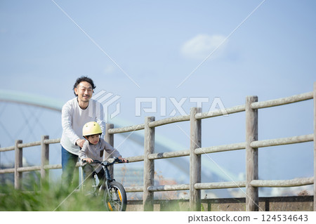 A child and his father practice riding a bicycle along the river. Good luck! 124534643