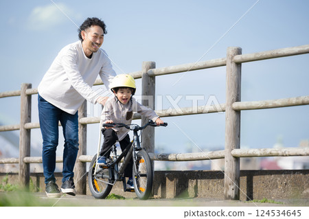 一個孩子和他的父親沿著河練習騎自行車。祝你好運！ 124534645