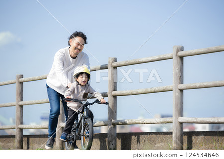 一個孩子和他的父親沿著河練習騎自行車。祝你好運! 一個孩子和他的父親沿著河練習騎自行車。祝你好運! 124534646