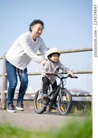 A child and his father practice riding a bicycle along the river. Good luck! A child and his father practice riding a bicycle along the river. Good luck! 124534647