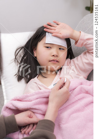 A girl resting wrapped in a blanket and her mother caring for her 124535161