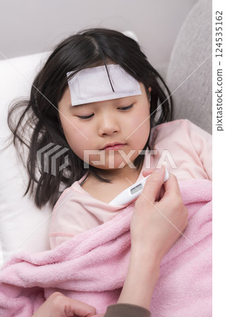 A girl resting wrapped in a blanket and her mother caring for her 124535162