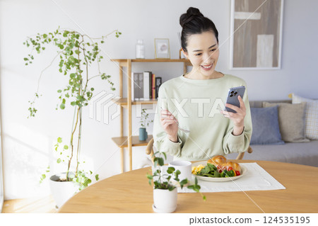 A woman eating while looking at her smartphone 124535195
