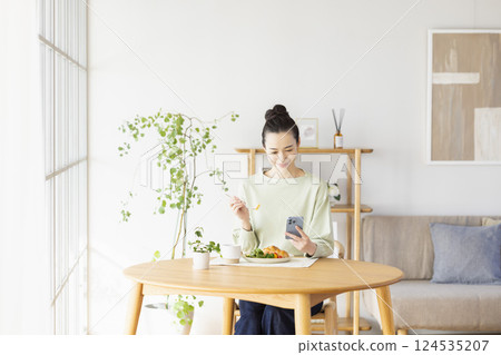 A woman eating while looking at her smartphone A woman eating while looking at her smartphone 124535207