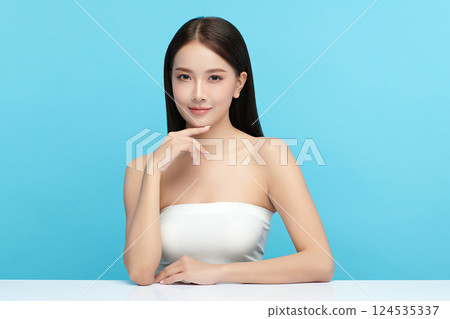 A beautiful young Asian woman with clean, fresh skin against a blue background. Skincare, facial treatment, cosmetology, beauty, and spa. An elegant portrait of an Asian woman. 124535337