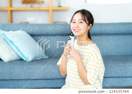 A young woman operating a smartphone in a room 124535764