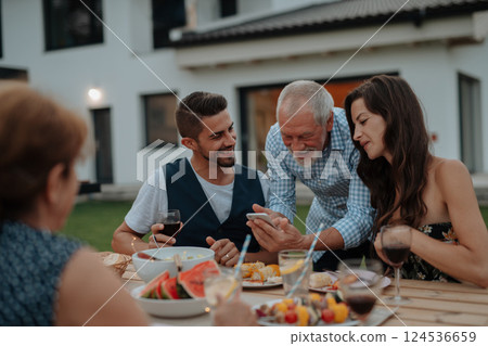 Older man showing photos on smartphone during spring family barbecue. 124536659